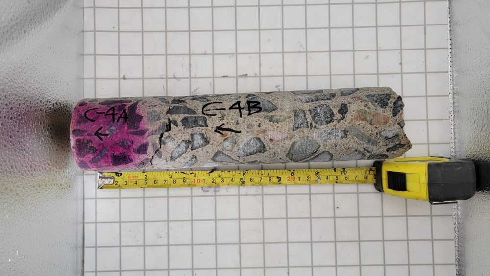 Concrete core, horizontally placed, over grid lines with a measuring tap alongside the bottom of the core